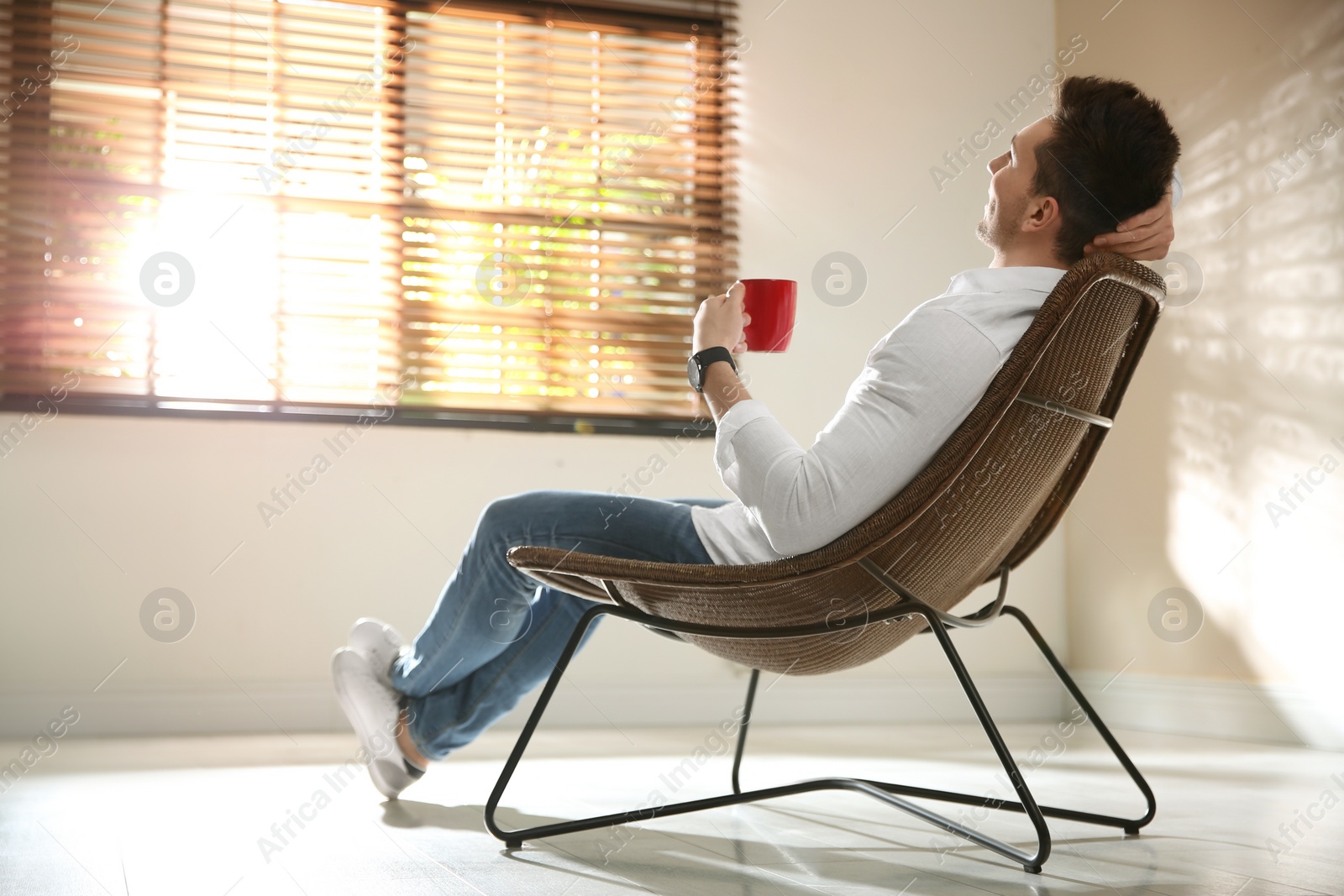 Photo of Young man with cup of drink relaxing near window at home. Space for text