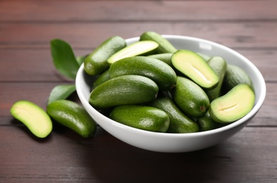 Fresh seedless avocados with green leaves in ceramic bowl on wooden table, closeup