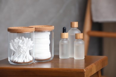 Cotton pads and swabs near cosmetic products on wooden stool in room