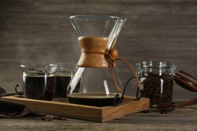 Glass chemex coffeemaker with coffee and beans on wooden table, closeup