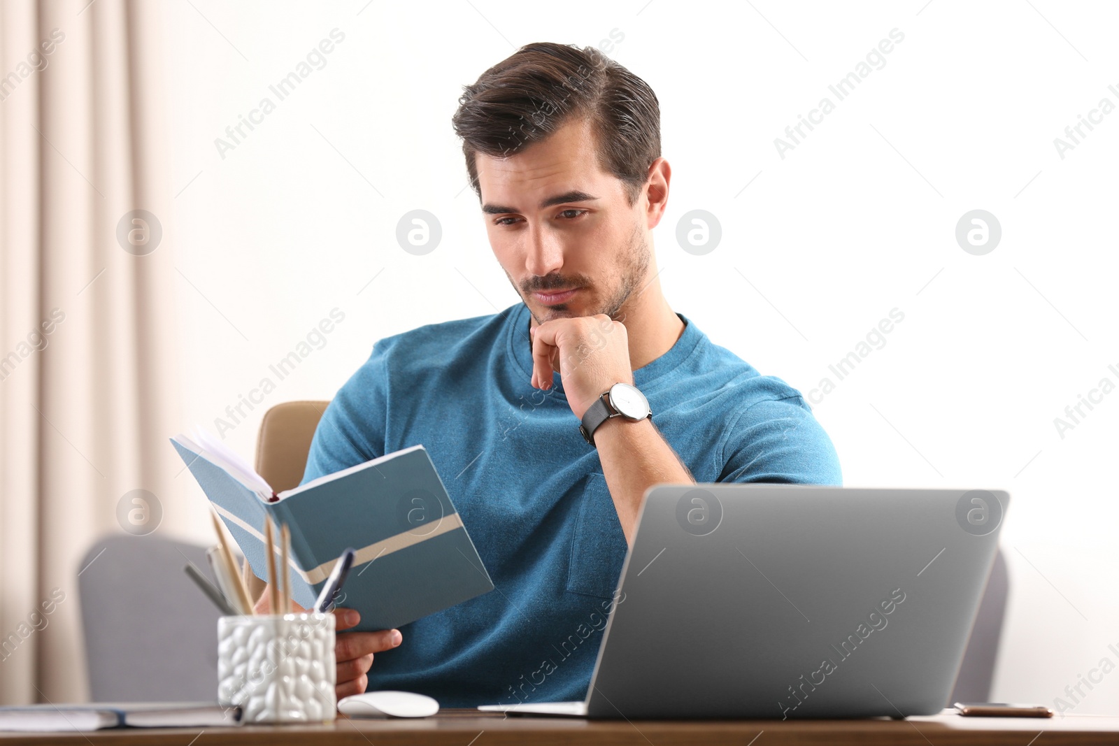 Photo of Handsome young man working with notebook and laptop at table in office