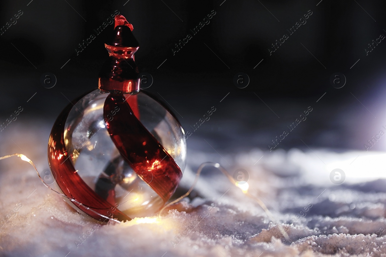 Photo of Christmas ball and fairy lights on white snow outdoors. Space for text