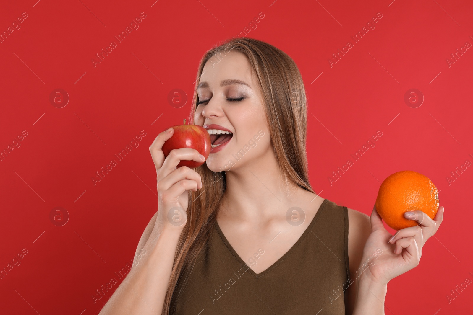 Photo of Young woman with apple and orange on red background. Vitamin rich food