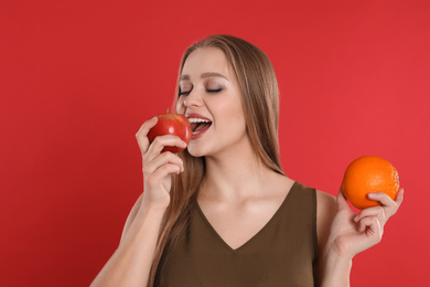 Young woman with apple and orange on red background. Vitamin rich food