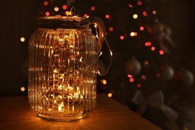 Photo of Jar with shiny lights and blurred Christmas tree on background