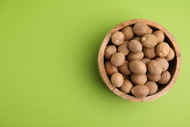Photo of Whole nutmegs in bowl on light green background, top view. Space for text