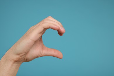 Photo of Man making half heart gesture with hand on light blue background, closeup