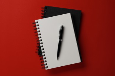 Photo of Notebooks and pen on red background, top view