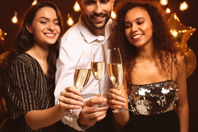 Happy friends celebrating New Year indoors, focus on hands with glasses of sparkling wine 