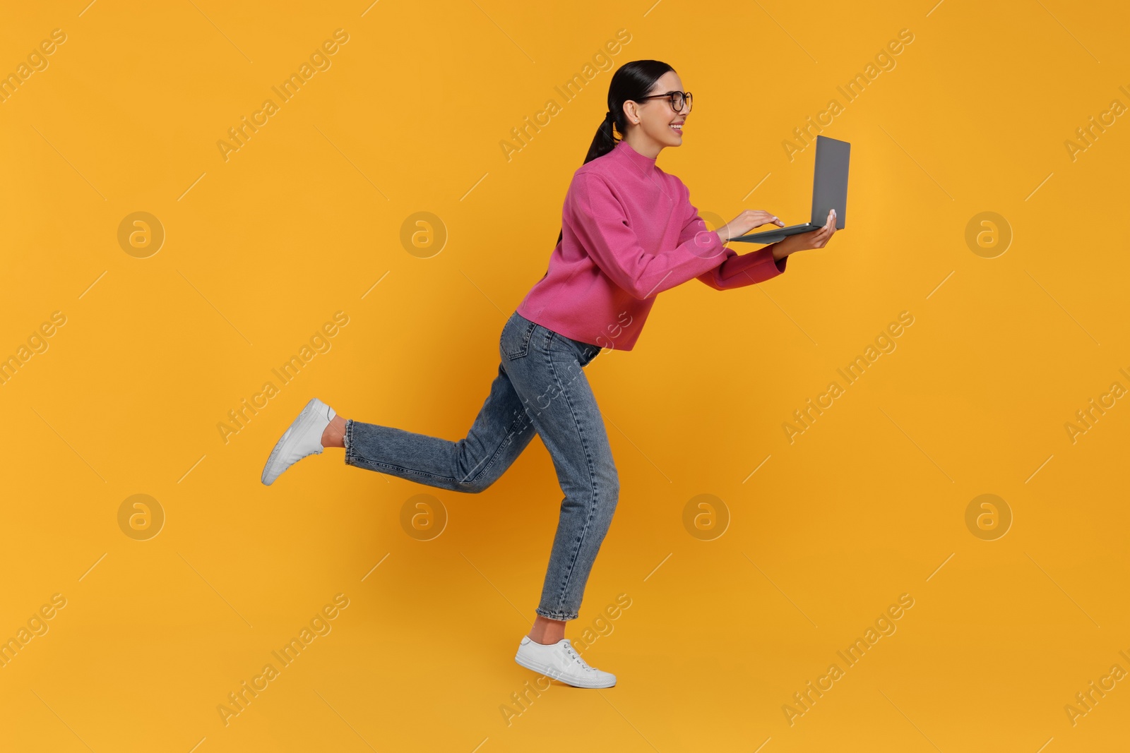 Photo of Happy woman with laptop running on orange background