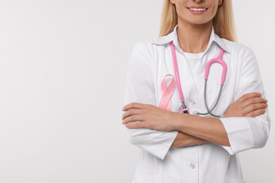 Photo of Doctor with pink ribbon and stethoscope on white background, closeup and space for text. Breast cancer awareness