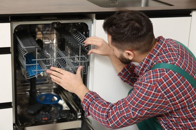 Photo of Serviceman repairing dishwasher cutlery rack indoors, closeup