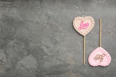 Photo of Chocolate heart shaped lollipops with word Love on grey table, flat lay. Space for text