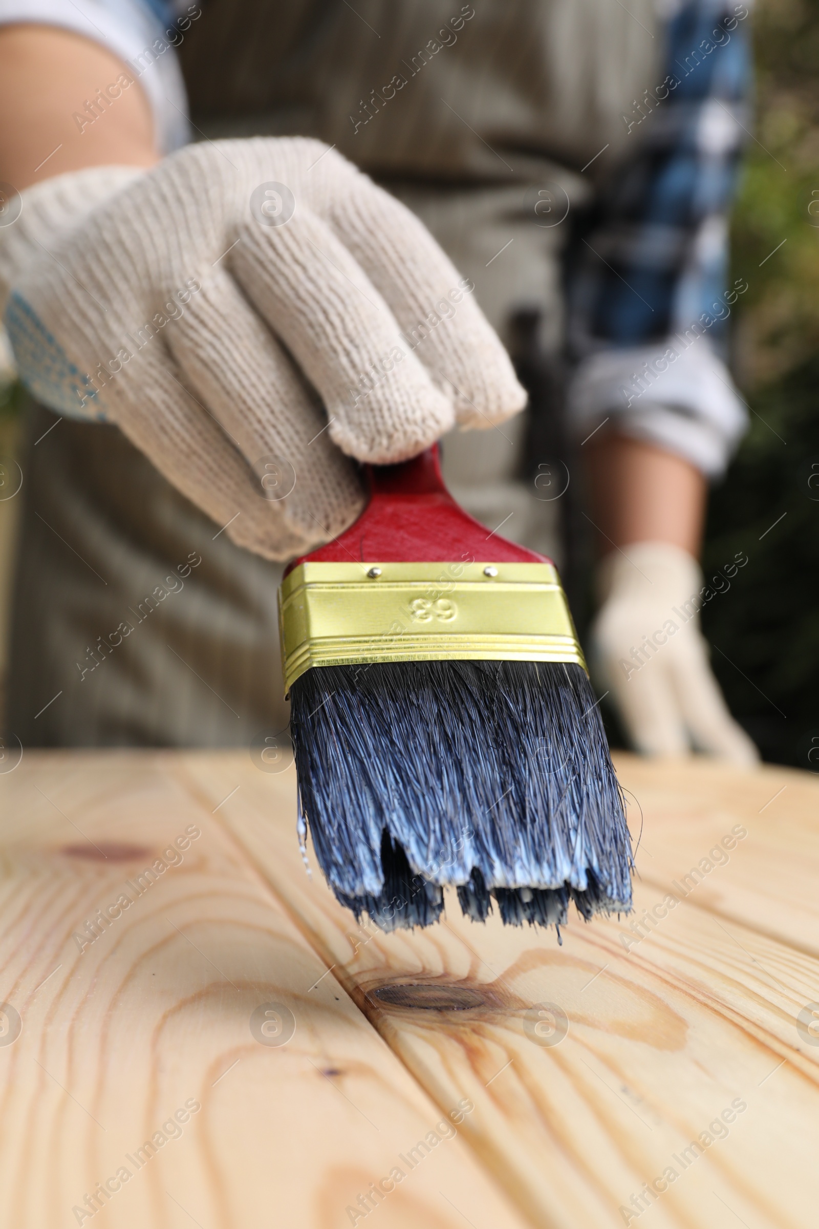 Photo of Man varnishing wooden surface with brush outdoors, closeup