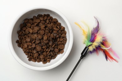 Photo of Dry cat food in bowl and pet toy on white background, flat lay