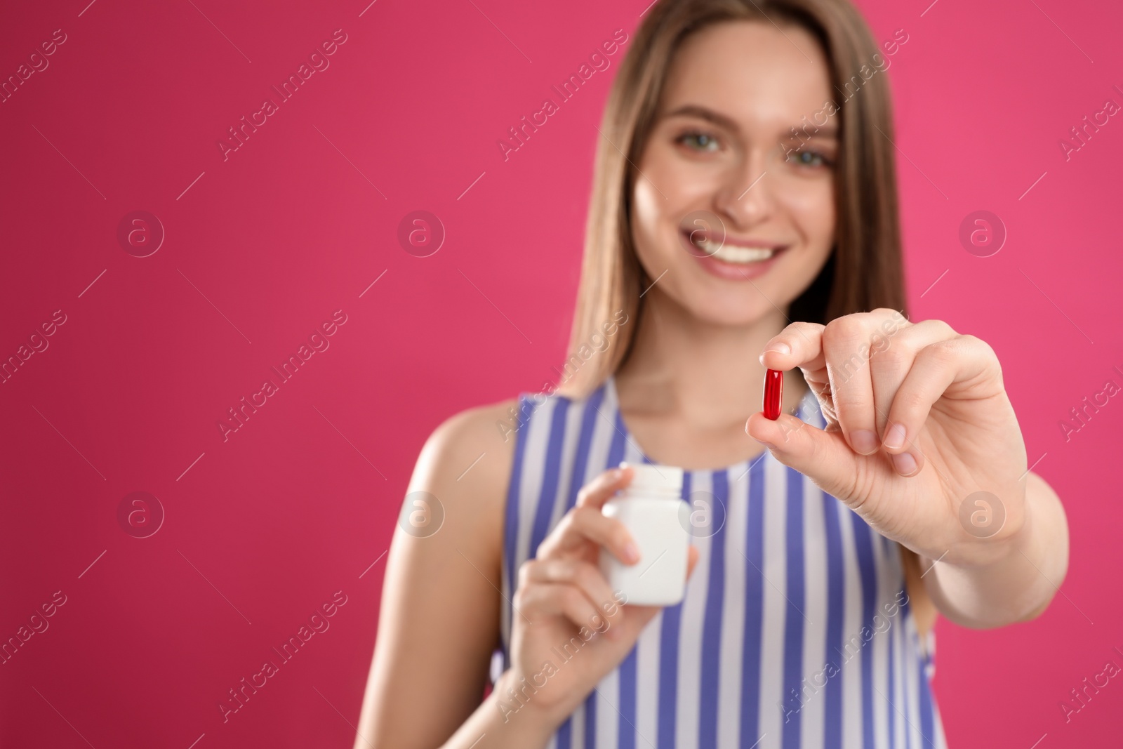 Photo of Young woman with vitamin pill against pink background, focus on hand