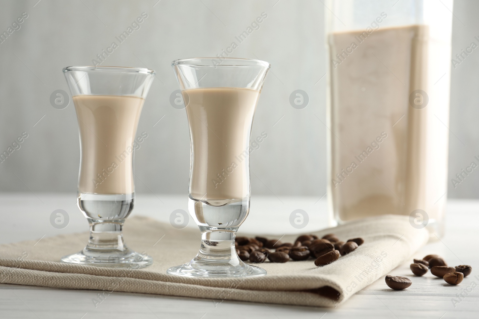 Photo of Coffee cream liqueur in glasses and beans on white wooden table