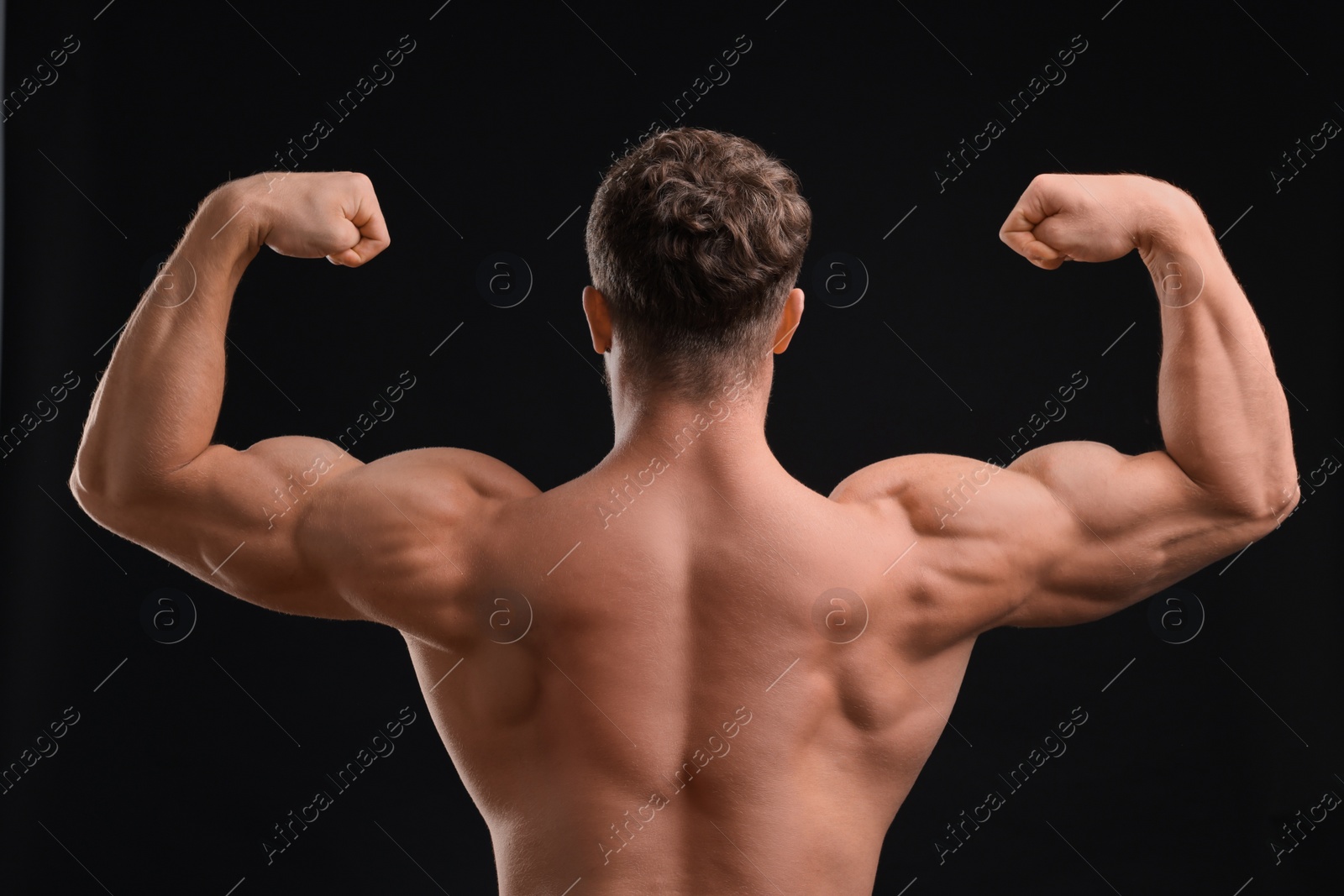 Photo of Muscular man showing his strength on black background, back view. Sexy body