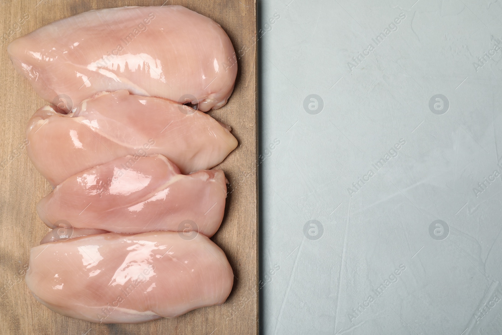 Photo of Wooden board with raw chicken meat on gray background, top view. Space for text