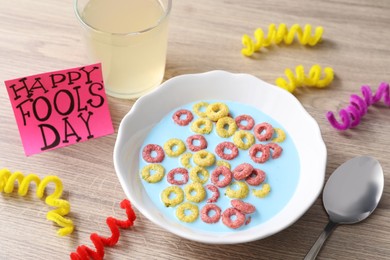 Photo of Plate of corn rings with light blue milk, drink and words Happy Fool's Day on wooden table