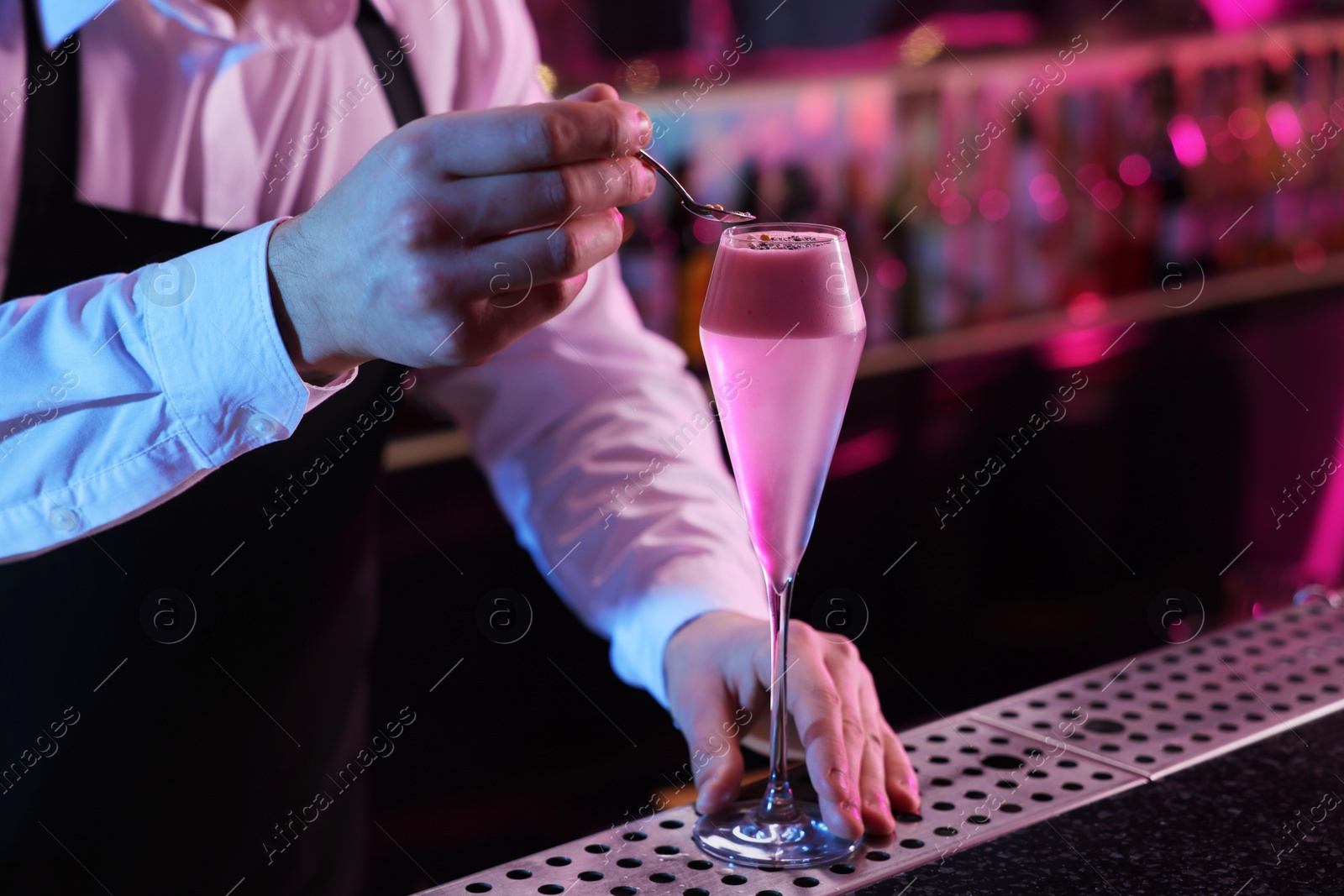 Photo of Bartender decorating fresh alcoholic cocktail with sprinkles at counter in bar, closeup