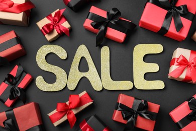 Photo of Word Sale and gift boxes on dark background, flat lay. Black Friday