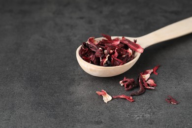 Photo of Hibiscus tea. Wooden spoon with dried roselle calyces on grey table. Space for text