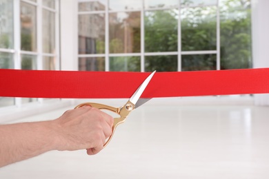 Man cutting red ribbon on blurred background. Festive ceremony