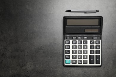 Calculator and pen on dark gray table, flat lay with space for text