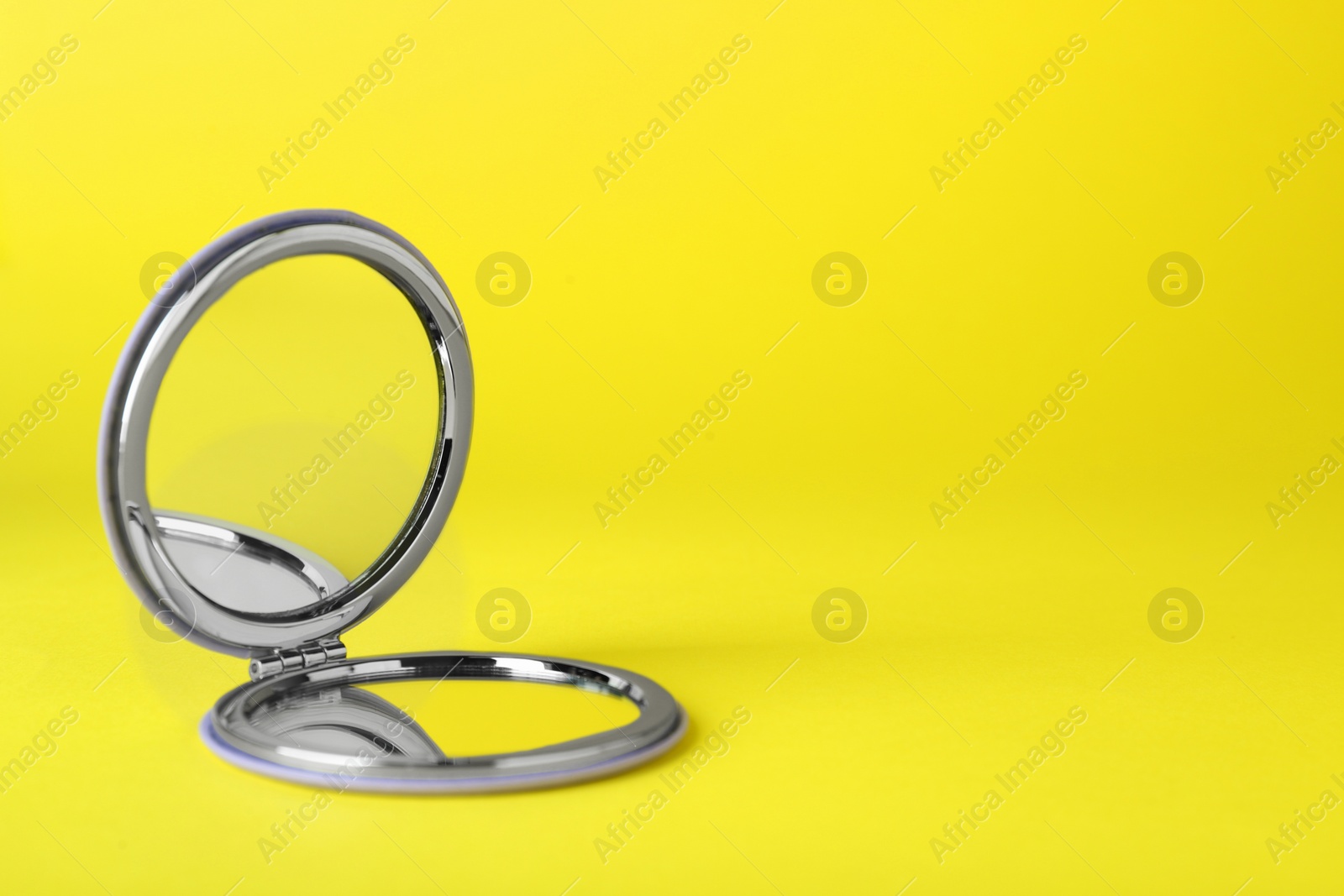 Photo of Stylish cosmetic pocket mirror on yellow background. Space for text