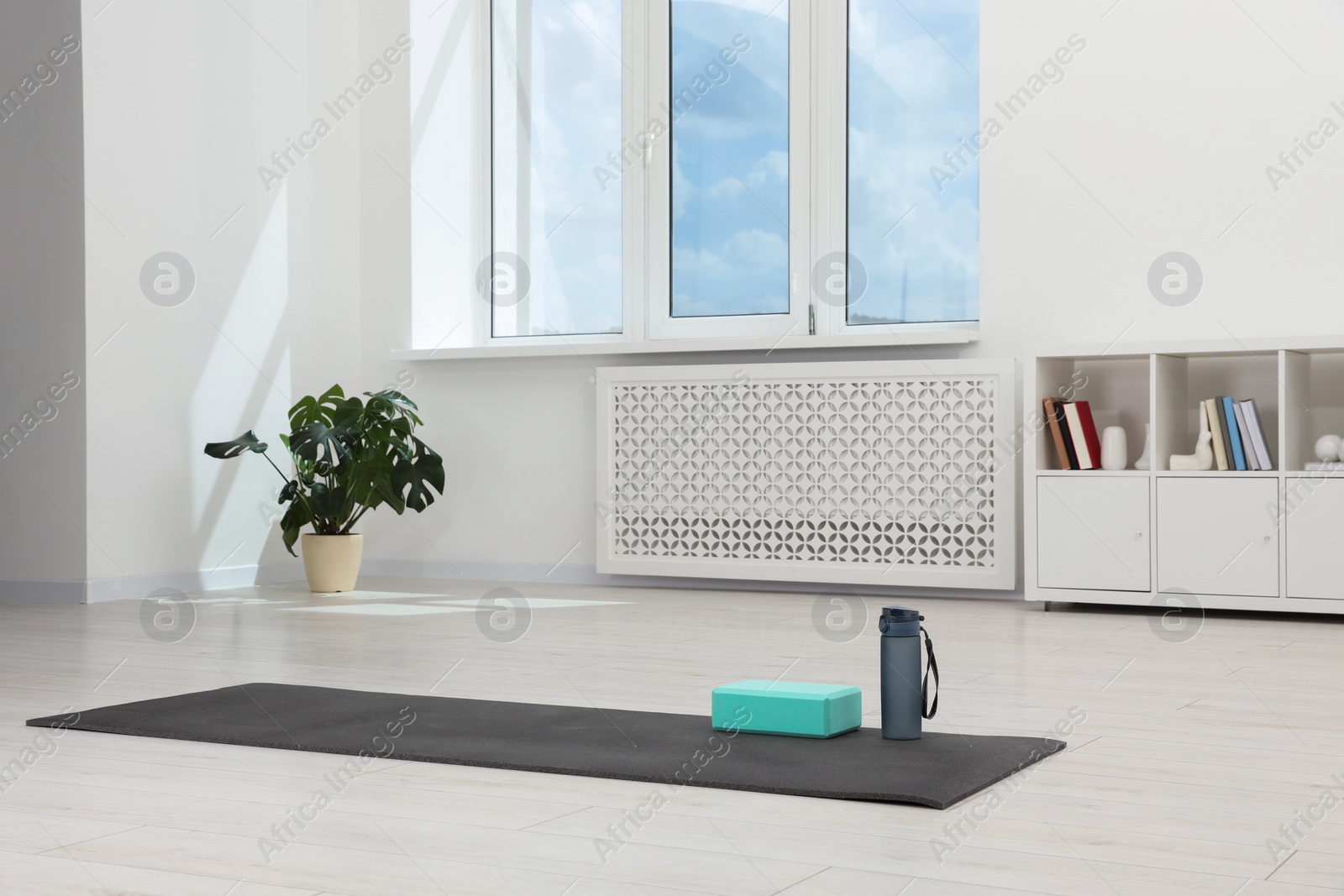 Photo of Exercise mat, yoga block and bottle of water on floor in room