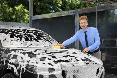 Businessman cleaning auto with sponge at self-service car wash