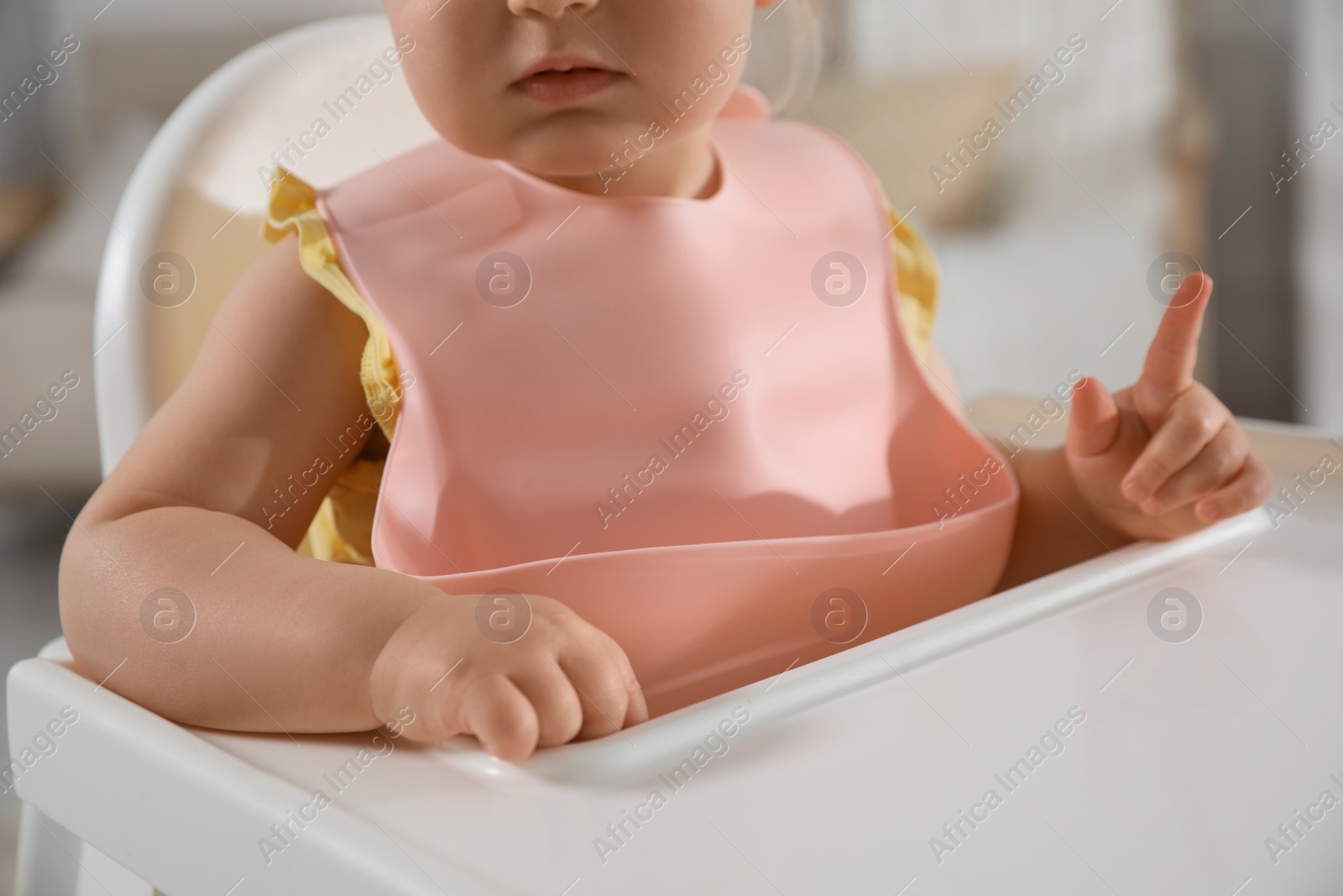 Photo of Cute little baby wearing bib in highchair indoors, closeup