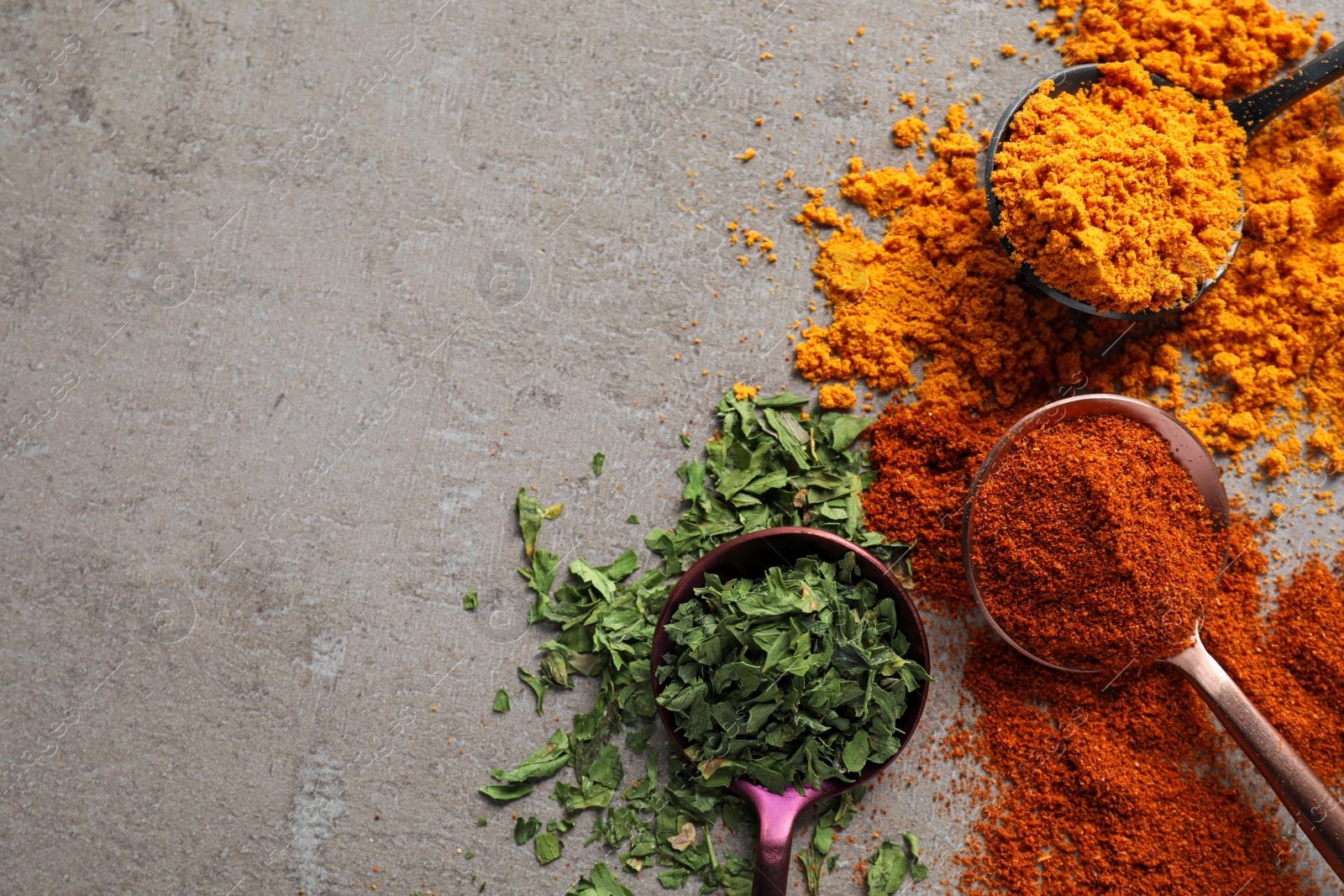 Photo of Different spices and spoons on grey textured table, space for text