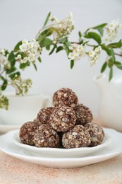 Delicious chocolate candies under blooming branch on beige table