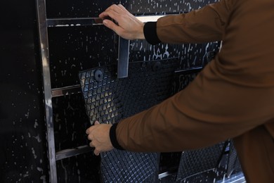 Photo of Man hanging auto mats with steel pegs for cleaning at self-service car wash, closeup
