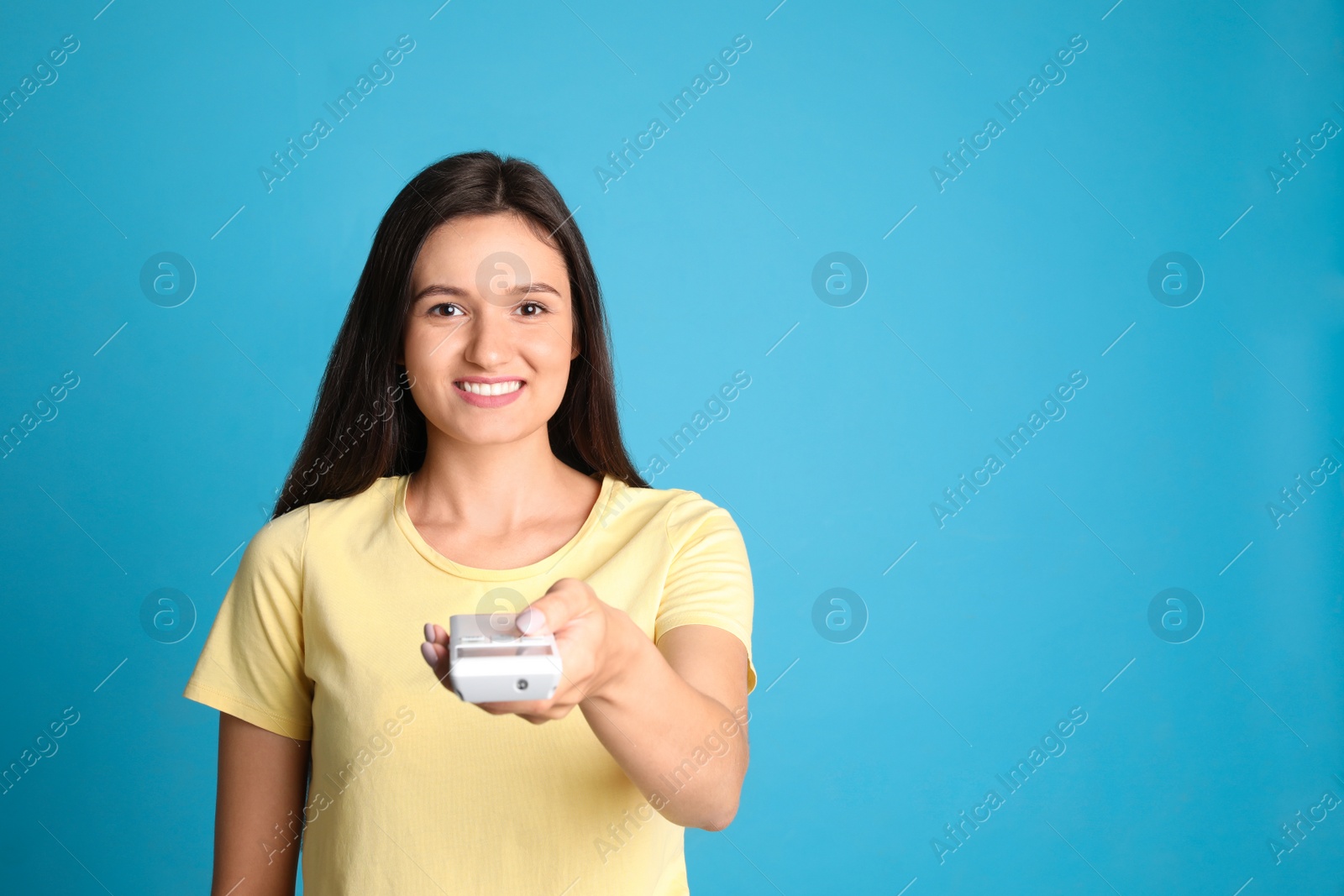 Photo of Happy young woman operating air conditioner with remote control on light blue background. Space for text