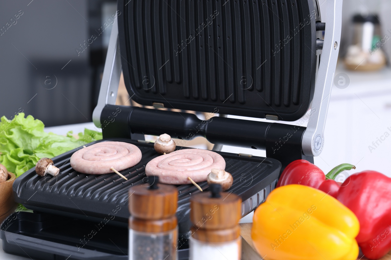 Photo of Electric grill with homemade sausages, mushrooms and vegetables on table