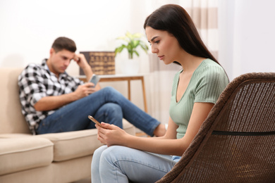 Photo of Couple addicted to smartphones ignoring each other at home. Relationship problems