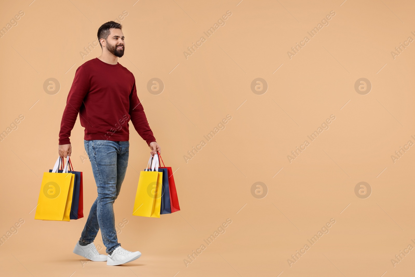 Photo of Smiling man with many paper shopping bags on beige background. Space for text