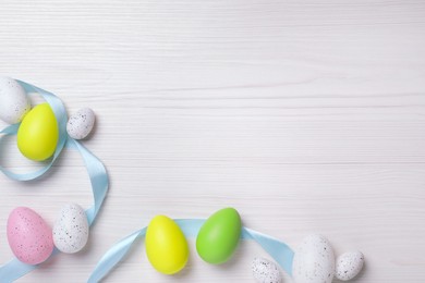 Flat lay composition with festively decorated Easter eggs on white wooden background. Space for text