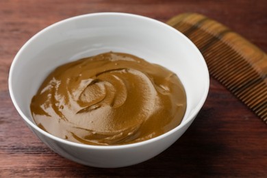 Photo of Bowl of henna cream on wooden table, closeup. Natural hair coloring