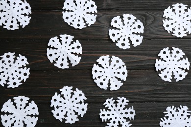 Photo of White paper snowflakes on black wooden table, flat lay