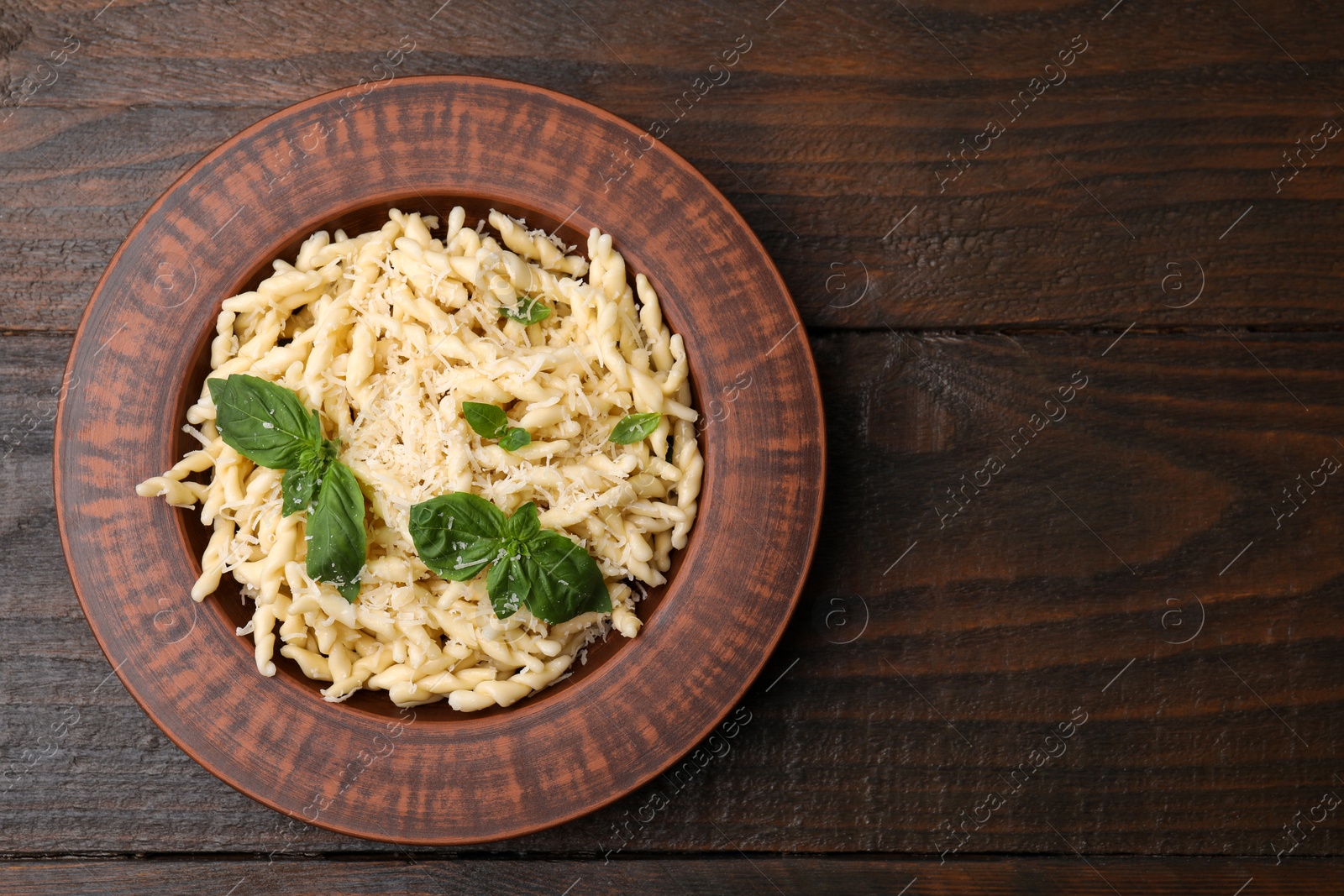 Photo of Plate of delicious trofie pasta with cheese and basil leaves on wooden table, top view. Space for text