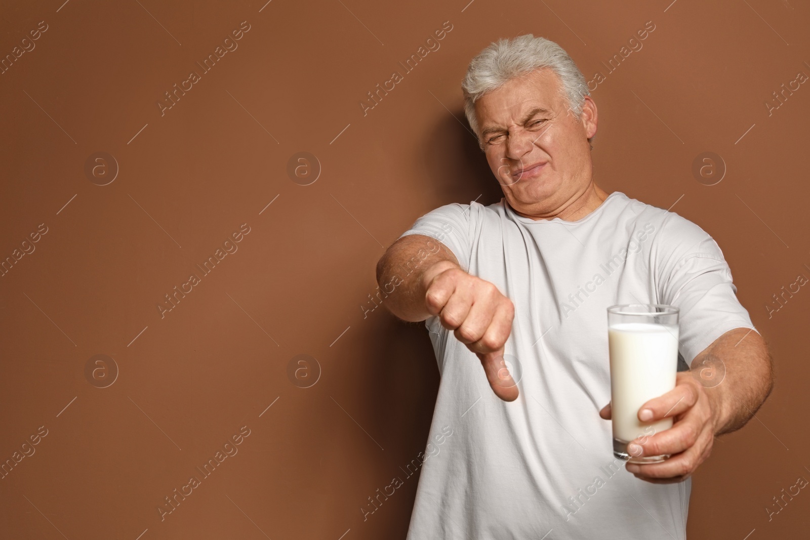 Photo of Mature man with dairy allergy holding glass of milk on color background