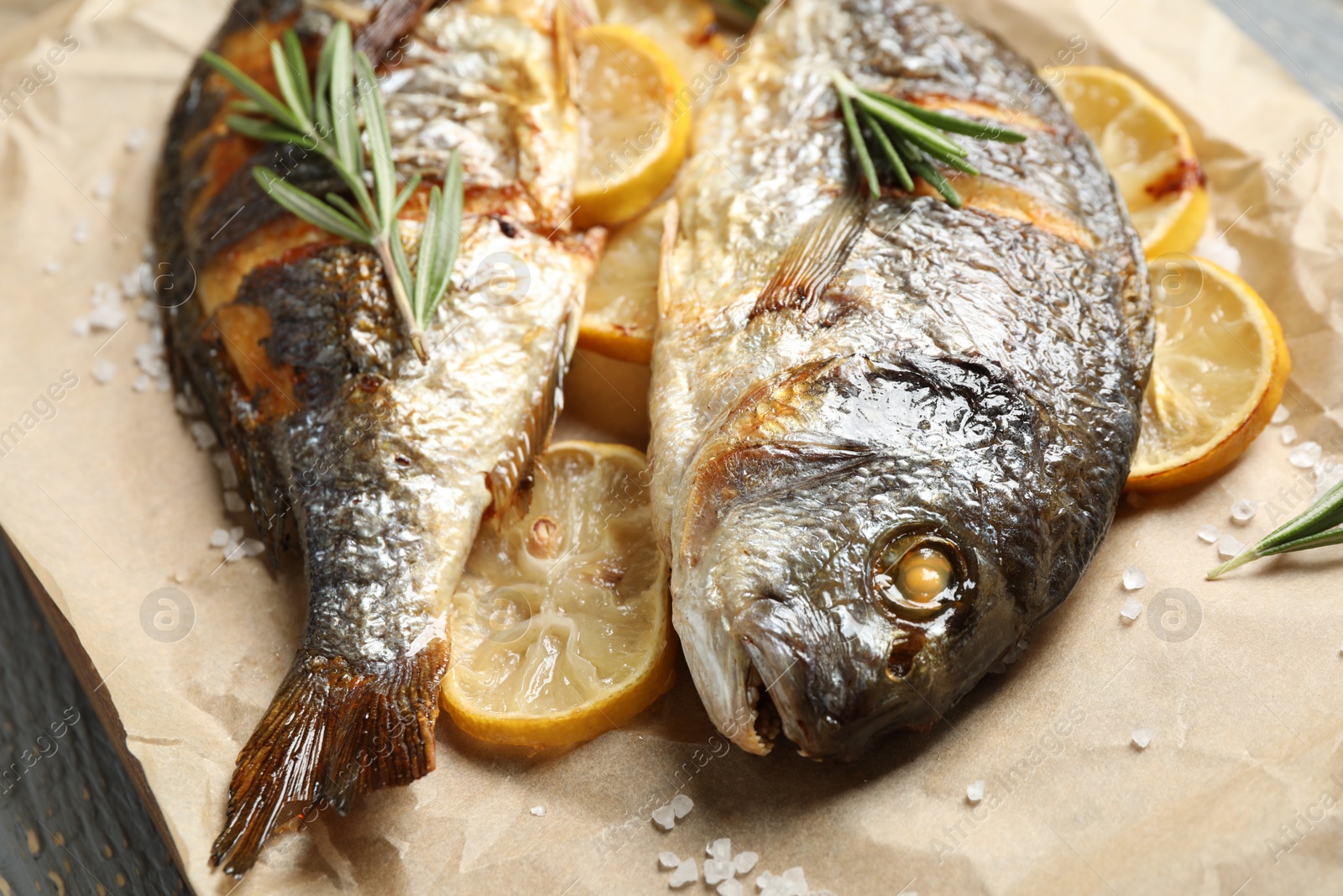 Photo of Delicious roasted fish with lemon on parchment paper, closeup
