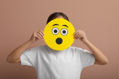 Photo of Little girl covering face with shocked emoji on pale pink background
