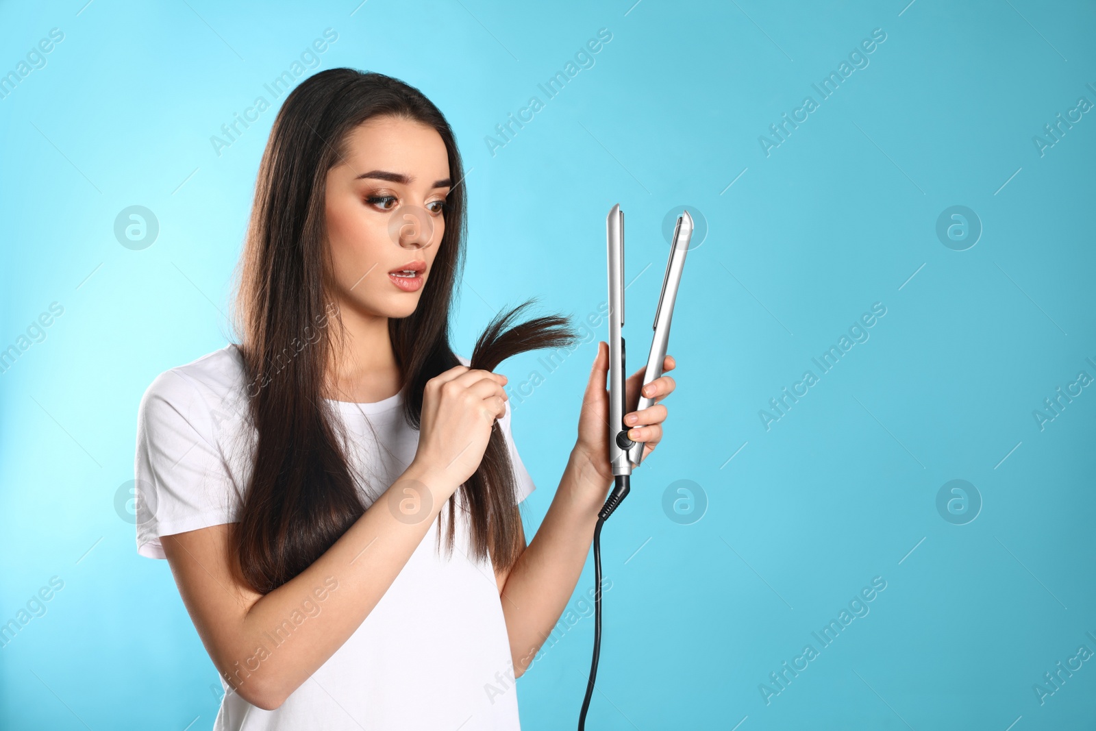 Photo of Emotional woman with hair iron on color background. Space for text