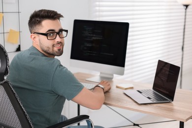 Photo of Happy young programmer working at desk in office