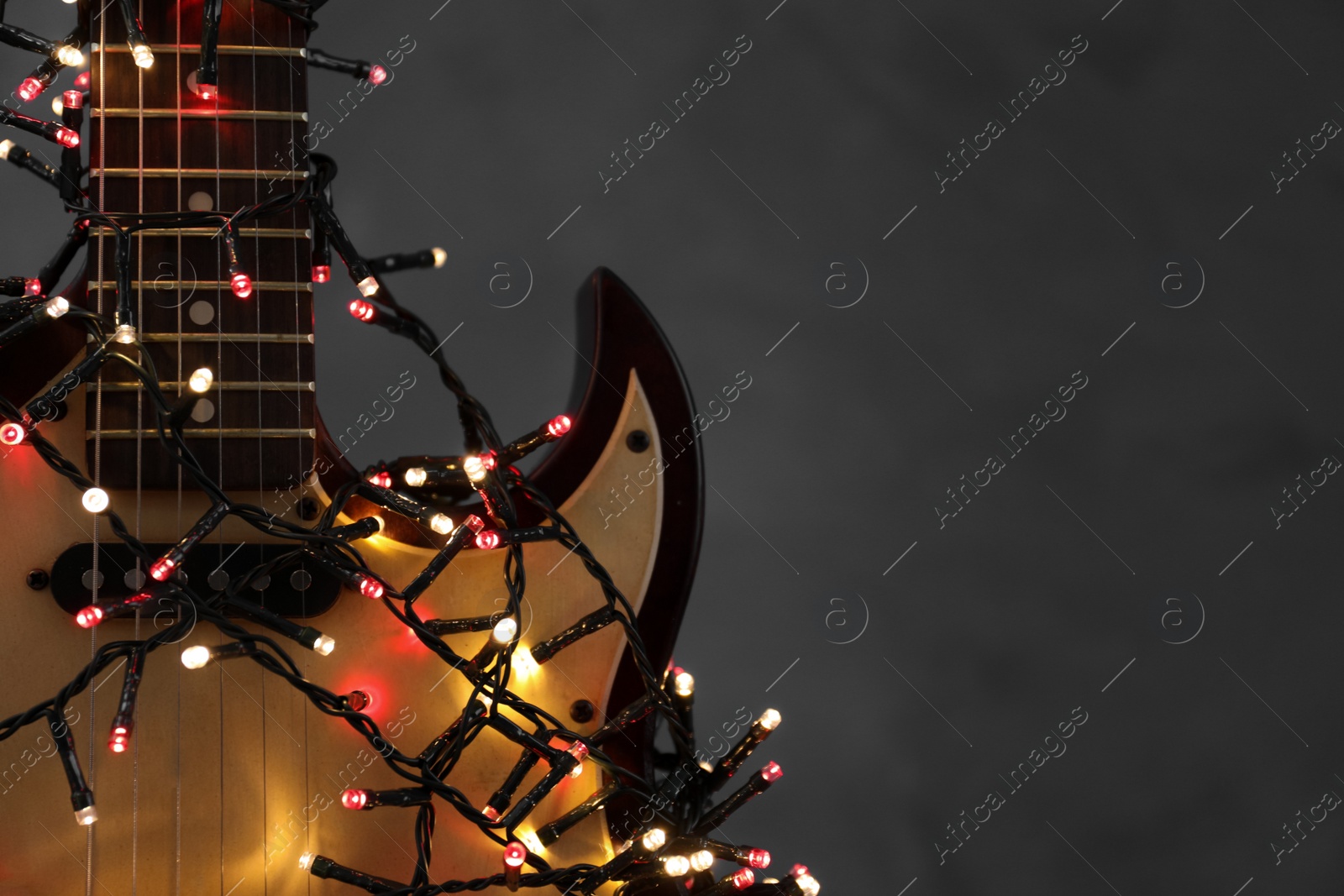 Photo of Closeup view of guitar with fairy lights on dark background, space for text. Christmas music